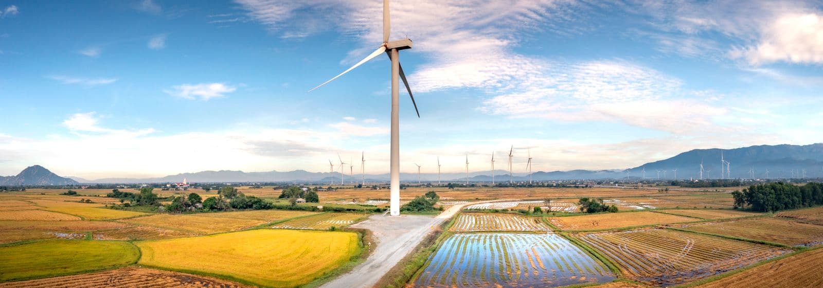 A wind turbine standing over green farmland under a bright blue sky