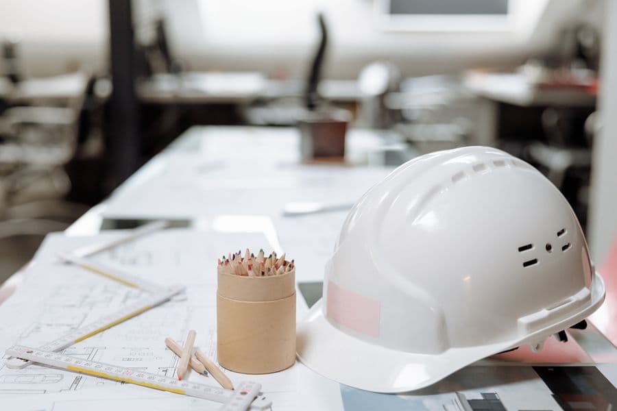 A white safety helmet resting on rolled architectural blueprints on a desk